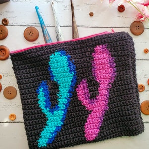 May include: A black crocheted zippered pouch with a pink and blue cactus design. The pouch is surrounded by wooden buttons.