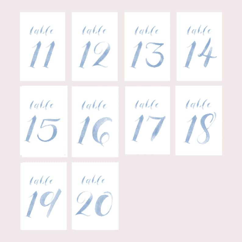 May include: Ten blue watercolor table number cards with the numbers 11 through 20 written in a cursive font. The cards are all the same size and shape, and they are arranged in two rows of five cards.