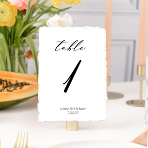 May include: White table number card with black calligraphy that reads "table 1" and the text "Jaime & Michael 7.22.25".