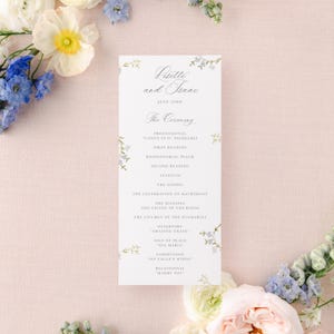 May include: A wedding ceremony program with a floral design featuring blue and green flowers. The program lists the order of the ceremony, including the processional, readings, and recessional. The text reads "Latte and Isaac, July 22nd, The Ceremony".