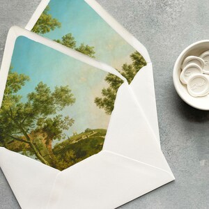 May include: A white envelope with a landscape scene printed on the front. The scene features a blue sky, green trees, and a small village in the distance.