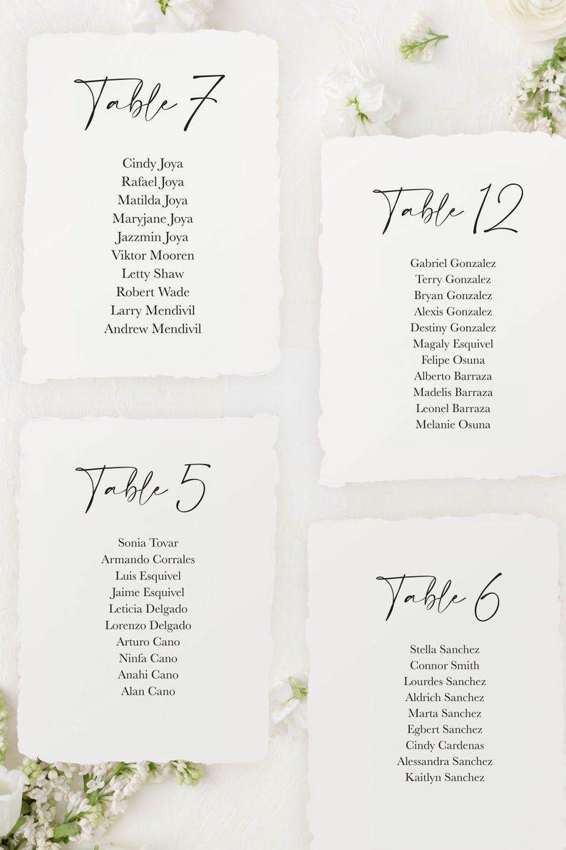 May include: A set of four white cards with black text listing table numbers and guest names for a wedding reception. The table numbers are 5, 6, 7, and 12.