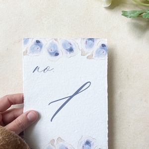 May include: A white card with a blue floral border and the text "no. 1" written in blue ink.