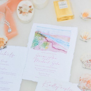 May include: A wedding invitation suite with a watercolor illustration of a beach scene. The invitation is printed on textured paper with pink and white text. The text reads "Together with their families,  Joime Ann and Michael John invite you to their wedding celebration the twenty-eighth of September five o'clock in the evening South Key Beach, Clearwater, FL. Kindly reply."