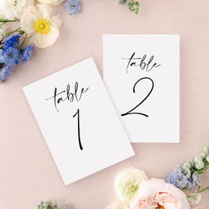 May include: Two white table number cards with black calligraphy. The top card says "table 2" and the bottom card says "table 1".