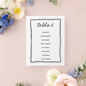 May include: A white card with a black border and the text "table 5" in black cursive writing. The card lists the names of eight guests: Mike Marte, Christina Marte, Rick Simmons, Raquel Simmons, Matt Mareci, Jenna Mareci, Joe Carnana, and Jackie Carnana.