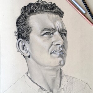 May include: A black and white pencil drawing of a man's face. The man has short, dark hair and is looking up and to the right. The drawing is signed "Elvira Vanni".