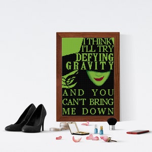 Peut inclure: Une impression encadrée avec un fond vert et une illustration noire et verte d'une femme au visage vert et au chapeau noir. Le texte sur l'impression est "Je pense que je vais essayer de défier la gravité et tu ne peux pas me faire tomber."