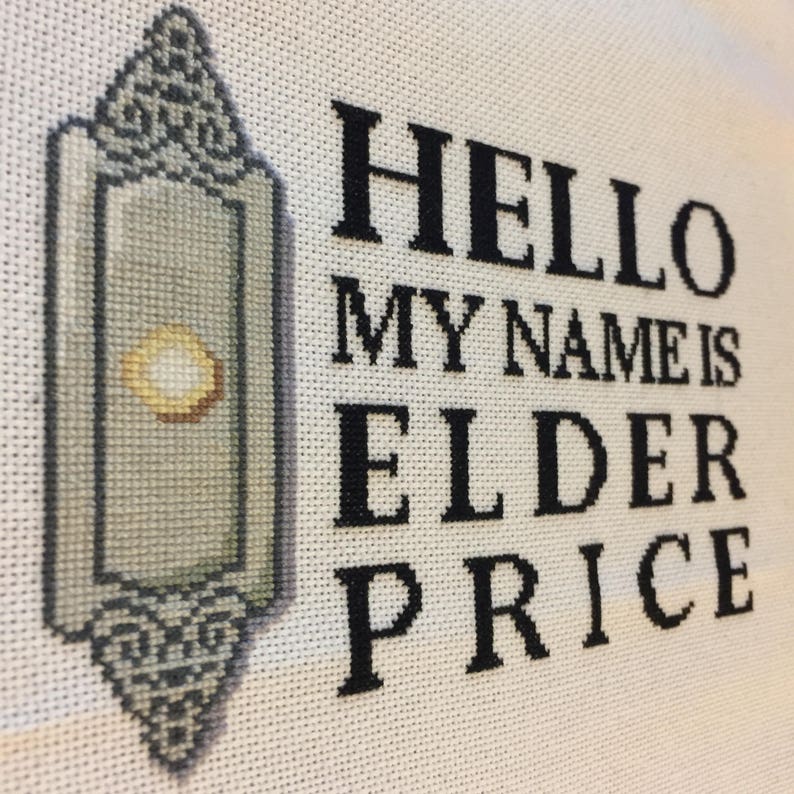 Puede incluir: Obra de arte de punto de cruz sobre tela blanca. El dise&ntilde;o presenta una linterna estilizada, verde claro y gris a la izquierda y el texto "HELLO MY NAME IS ELDER PRICE" en letras negras y en negrita a la derecha. La pieza es probablemente hecha a mano.