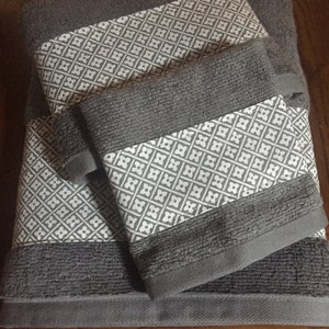 May include: A set of grey bath towels featuring a geometric white and grey pattern. The towels are folded and stacked, displaying the patterned border. The towels are made of a soft, absorbent material, ideal for bathroom use.