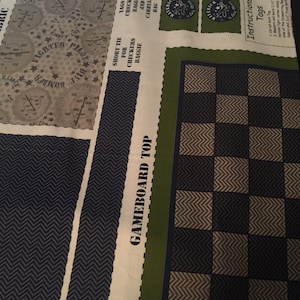 Può includere: Un pannello di tessuto bianco con un motivo a scacchi verde e nero. Il pannello ha un testo che recita "GAMEBOARD TOP" e "Instructions For Tags". Il testo include istruzioni per tagliare le etichette e misurarle. Il pannello di tessuto è progettato per un gioco o un progetto di artigianato.