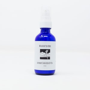May include: A cobalt blue glass bottle with a white pump top. The label reads "Wildcrafted Rebel" above a mountain and plant graphic. Below, it says "Lavender Sunscreen SPF 30+" and "2 fl oz."