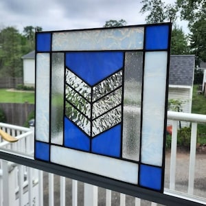 May include: A stained glass window with a geometric design featuring a blue chevron shape surrounded by white and clear glass.