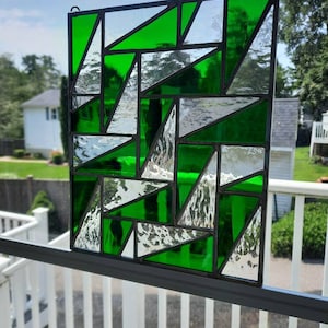 May include: A rectangular stained glass panel with a geometric design. The panel features a pattern of green and clear glass pieces, framed by black metal. The glass is arranged in a series of triangles and other shapes.
