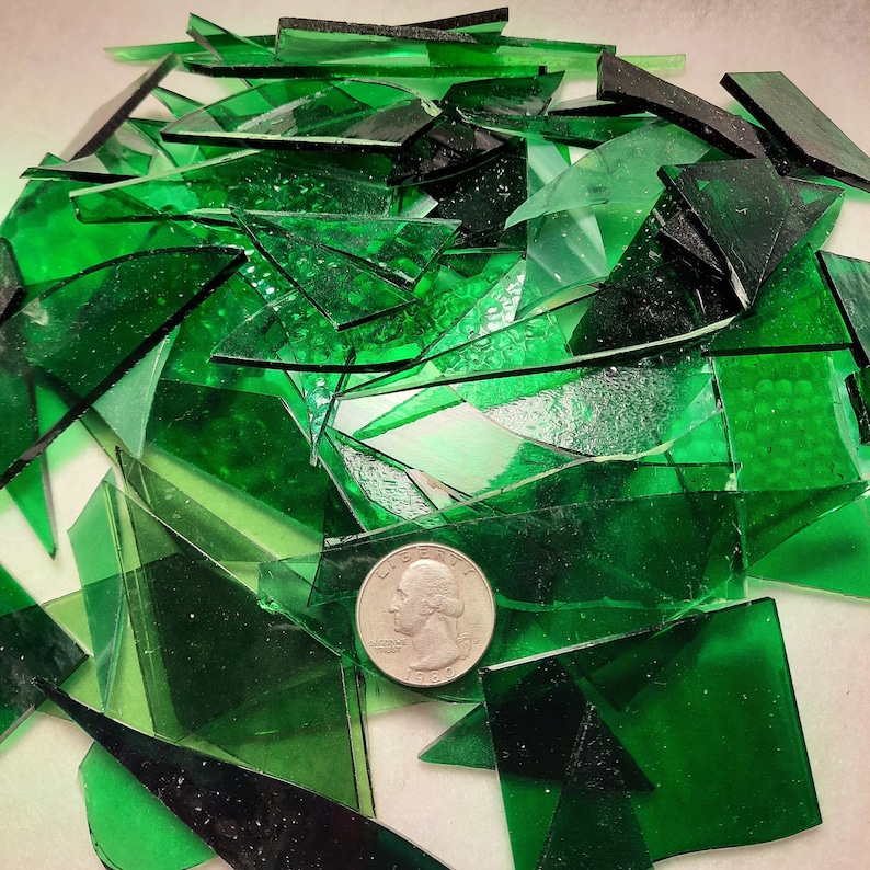 May include: A pile of green glass shards, some with a textured surface, with a silver coin on top.