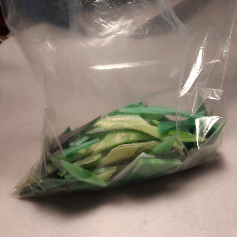 May include: A plastic bag filled with green and light green glass pieces. The glass pieces are various shapes and sizes.