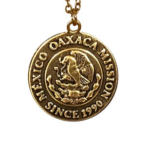 May include: Gold necklace with a round pendant featuring the Coat of Arms of Mexico and the text "Oaxaca Mission Mexico Since 1990".