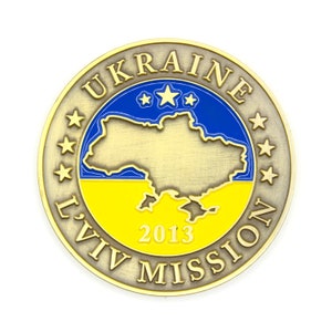 May include: A gold-colored metal coin with the words "UKRAINE LVIV MISSION 2013" around the edge. The center of the coin features a blue and yellow map of Ukraine with three gold stars.