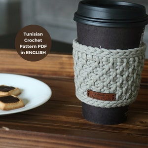 Peut inclure: Un manchon de tasse à café en crochet gris avec une étiquette en cuir marron qui dit "Handmade by Naomi Knits".