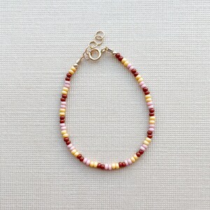 May include: A delicate bracelet made with small, colorful beads in shades of yellow, pink, and brown. The bracelet has a gold clasp.