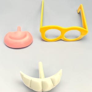 May include: A selection of novelty costume items, including yellow glasses, a pink nose, and white teeth. The plastic pieces are designed for fun and play, perfect for dressing up or themed events.