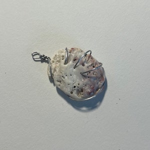May include: A white and pink seashell with a wire wrapped around it. The wire is shaped into a cage-like design.