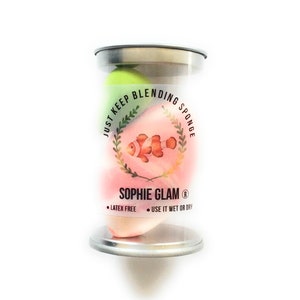 Può includere: Un contenitore di plastica trasparente con un coperchio argentato contiene tre spugne per il trucco colorate per sfumare. Le spugne sono etichettate "Just Keep Blending Sponge" con un pesce dei cartoni animati e il testo "Sophie Glam® Latex Free Use It Wet Or Dry".