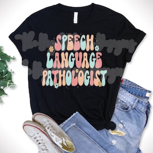 May include: Black t-shirt with a retro-style graphic that says "Speech Language Pathologist" in pastel colors with flowers and a smiley face.