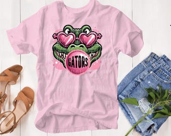 May include: Pink t-shirt with a cartoon alligator wearing heart-shaped sunglasses and blowing a bubble that says "GATORS".