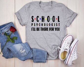 May include: Gray t-shirt with the text "S.C.H.O.O.L. PSYCHOLOGIST I'LL BE THERE FOR YOU" in black. The text is in a stylized font with colorful dots between the letters.