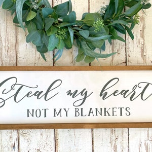 May include: A wooden sign with a white background and a brown frame. The sign says "Steal my heart not my blankets" in black cursive lettering.