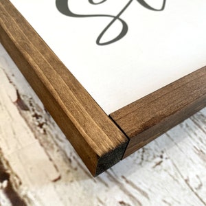May include: Close-up of the corner of a wooden frame with a dark brown stain. The frame is made of solid wood and has a smooth finish.