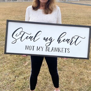 May include: A white wooden sign with black lettering that reads "Steal my heart not my blankets".