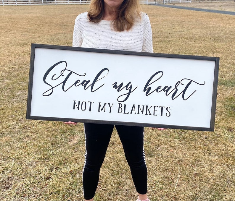 May include: A white wooden sign with black lettering that reads "Steal my heart not my blankets".