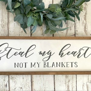 May include: A white wooden sign with a brown frame, featuring the text "Steal my heart not my blankets" in a cursive font.