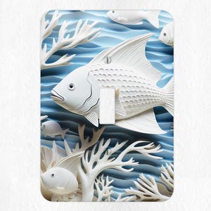 May include: White ceramic fish and coral design light switch cover. The fish are sculpted in a 3D style and appear to be swimming in a blue ocean.