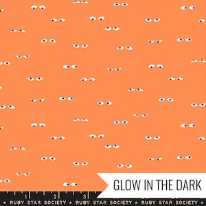 May include: Orange fabric with a repeating pattern of white eyes. The fabric glows in the dark. The text "GLOW IN THE DARK" is printed at the bottom of the image. The text "RUBY STAR SOCIETY" is printed at the bottom of the image.