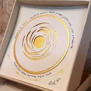 May include: A white box with a gold-colored design on the lid. The design is a circle with a spiral pattern inside. The box is open and the lid is resting on the bottom of the box. The box is sitting on a stone surface.