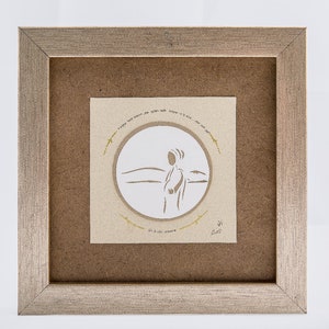 May include: A framed paper cut-out artwork featuring a silhouette of a person standing in a landscape. The artwork is surrounded by a circle of text in Hebrew and a gold frame.