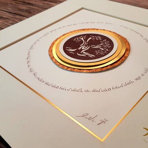 May include: A framed artwork featuring a brown tree with white branches and leaves, surrounded by a gold circle with Hebrew text. The artwork is signed "Eli" and has a gold frame.