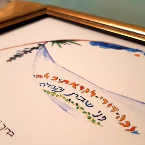 Op de afbeelding: Een ingelijst aquarel schilderij met een blauwe en witte halve maan vorm met Hebreeuwse tekst in oranje, geel en groen. De tekst luidt "פע שבת קבלה בריך אינהה אל קינו מלך העולם אשר קדשנו במצותי ועזע להדליק נדל שבית".