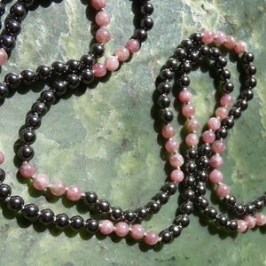 May include: A beaded necklace with alternating black and pink beads. The necklace is made of two strands of beads, one black and one pink.