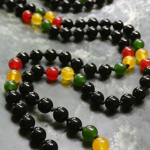 May include: A black onyx beaded necklace with green, yellow, and red gemstone accents. The necklace is made with black cord and features a silver clasp.