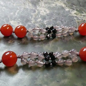 May include: A necklace made with carnelian, grey agate, and black faceted beads. The necklace is made with a double strand of beads and has a simple knot design.