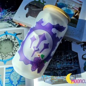 May include: A frosted glass jar with a purple and white design featuring a stylized image of a trident and grapes. The jar has a wooden lid.