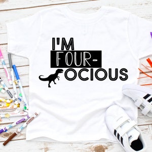 Puede incluir: Camiseta blanca con texto negro que dice "I'm Four-ocious" con una silueta de dinosaurio negro.