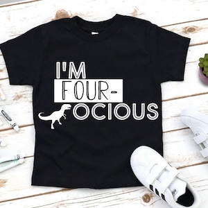 Puede incluir: Camiseta negra con texto blanco que dice "I'm Four-ocious" y una ilustraci&oacute;n de dinosaurio blanca.