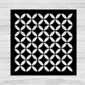 May include: A black square with a repeating pattern of white, four-petal flower shapes. The design is symmetrical and creates a visually interesting texture. The background is a light gray wood grain.