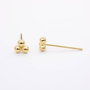Könnte beinhalten: Ein Paar goldene Ohrstecker, jeder mit drei kleinen, runden Perlen, die zusammen gruppiert sind.