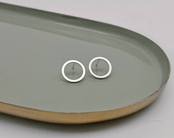 Könnte beinhalten: Ein Paar silberne Kreis-Ohrstecker. Die Ohrringe sind schlicht und minimalistisch, mit einer glatten, polierten Oberfläche.